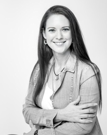 Black and white photo of a smiling woman with long hair wearing a light-colored denim jacket and a white top, sitting with her arms crossed in front of her. This picture captures the essence of a life coach in Pretoria East, radiating confidence and warmth.